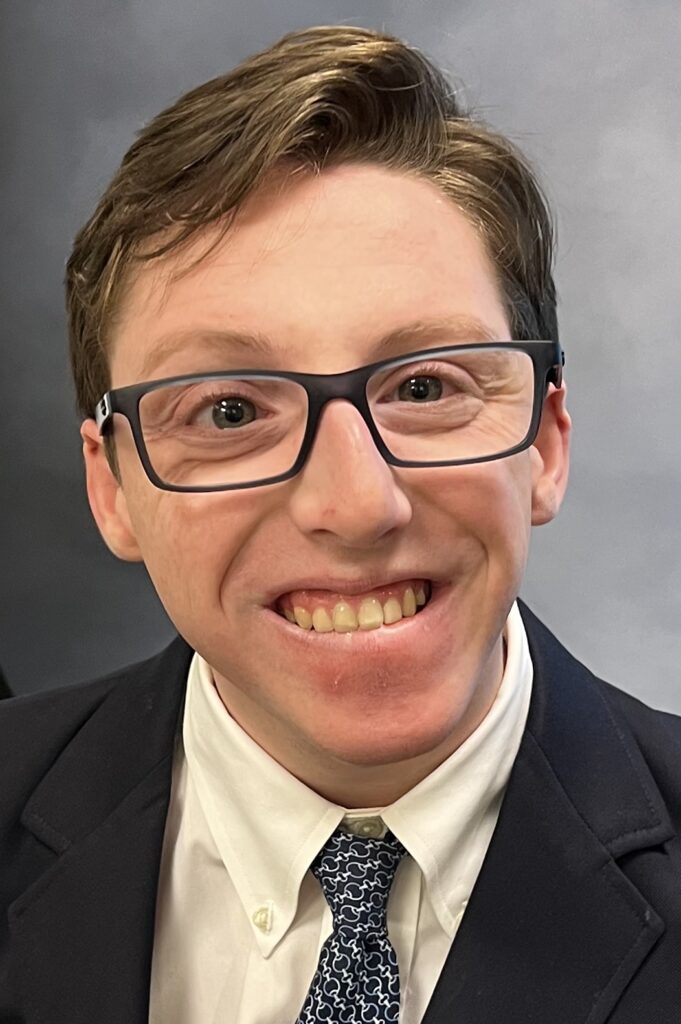 man with brown hair, glasses, wearing a suit
